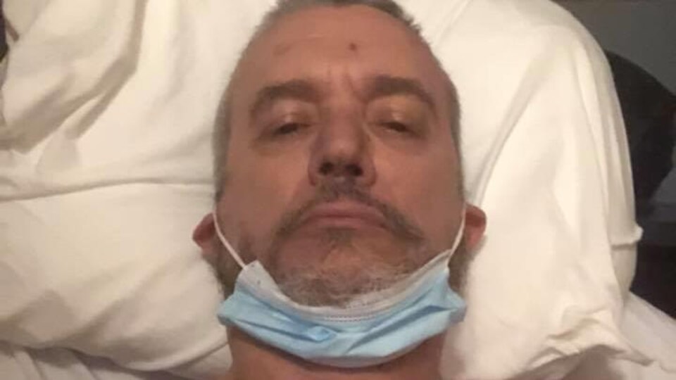 Un homme portant un masque chirurgical au cou est couché dans un lit d'hôpital.