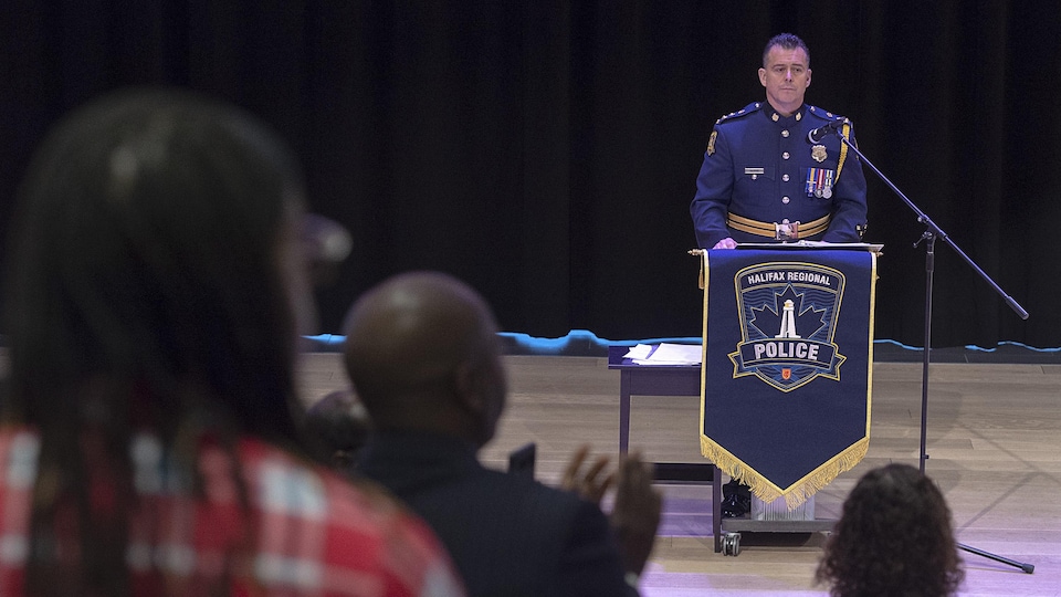 Des gens se lèvent et applaudissent le chef de police en uniforme devant un lutrin.