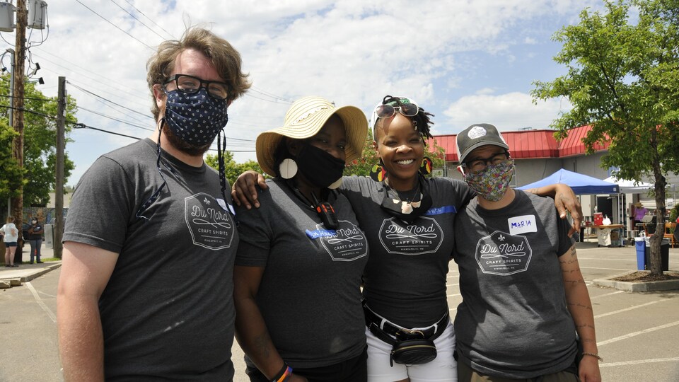 Quatre personnes, dont trois portant un masque, posent pour la caméra. Ils portent tous le même chandail.