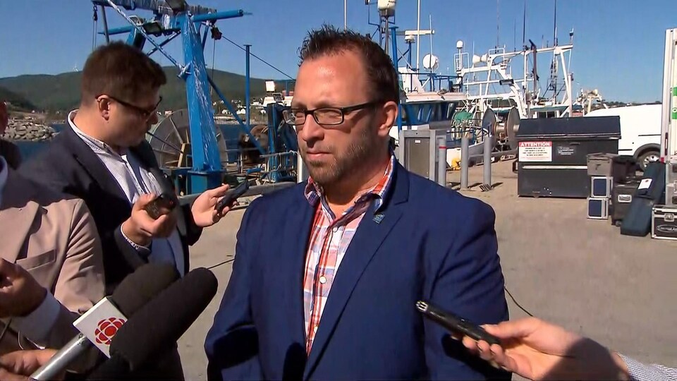 Daniel Côté répond aux questions de journalistes devant un bateau de pêche.