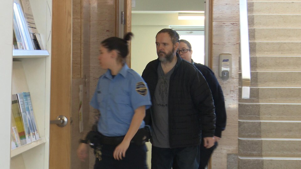 Deux agents de sécurité escortent un suspect dans un palais de justice.