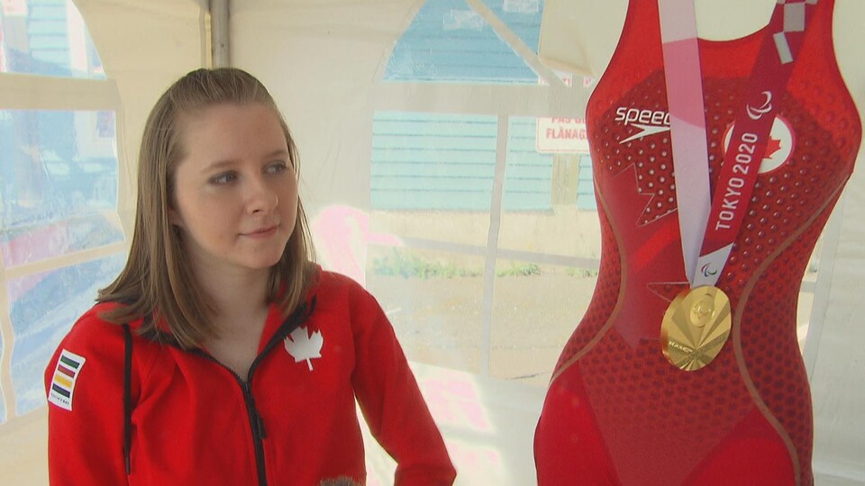 La jeune athlète à côté d'un mannequin couvert de son maillot et exhibant sa médaille d'or.