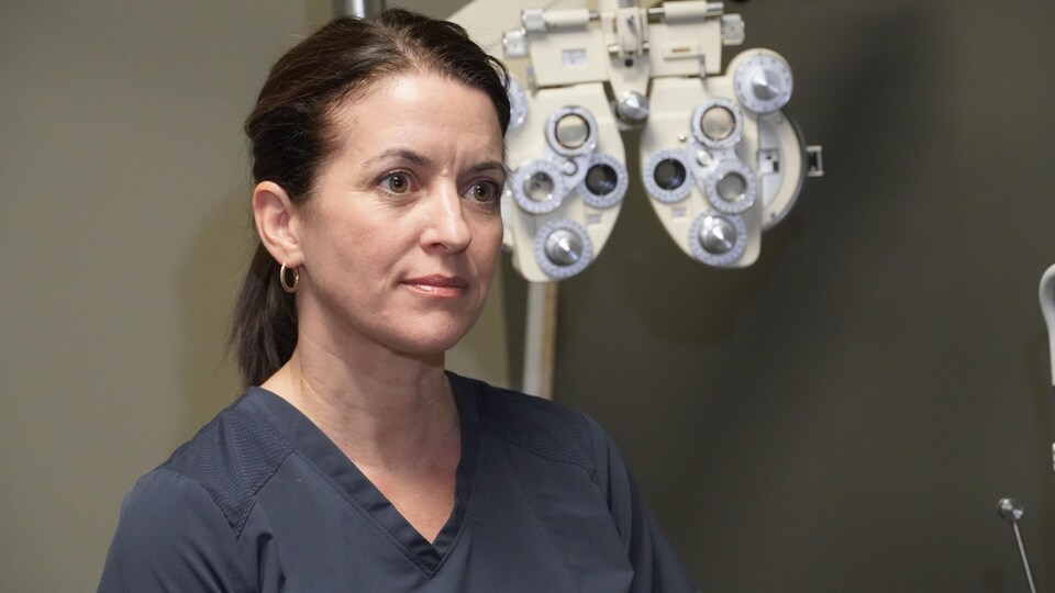 Une dame regarde devant elle, debout devant un appareil d'optométrie servant à faire un examen de la vue.