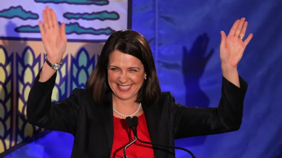 Danielle Smith salue des partisans en levant les bras, devant un podium.
