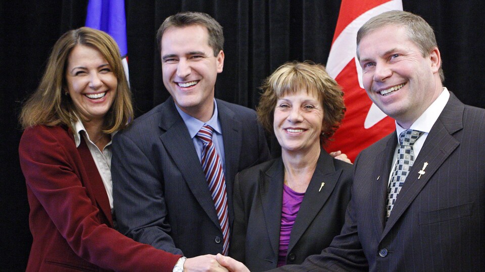 Les quatre politiciens se tiennent la main en souriant à la caméra.