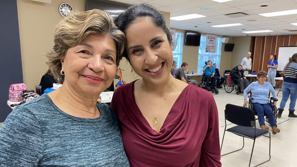 Deux femmes sourient. Elles se trouvent dans une salle communautaire.
