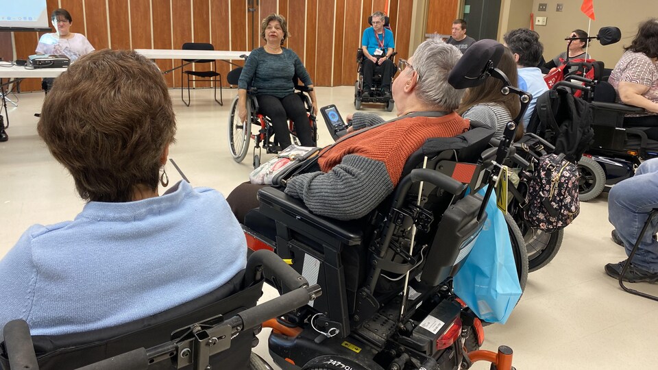 Une professeure se trouve dans un fauteuil roulant devant un groupe.