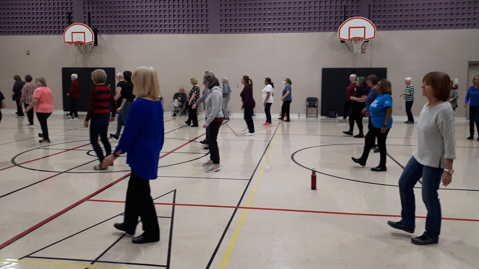 Des hommes et des femmes, soient des aînés ou des retraités, dansent sur un terrain de basketball lors des classes animées par Nicole Côté.