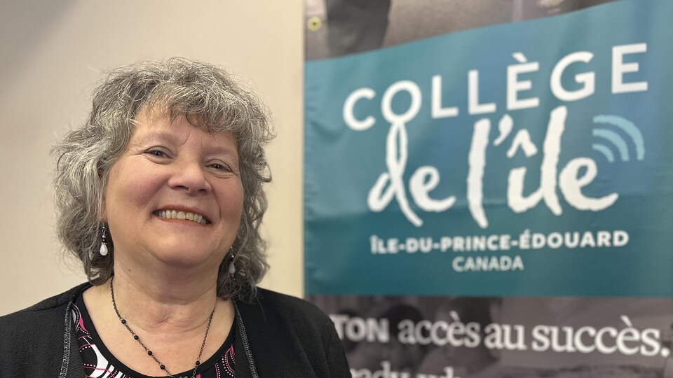 Darlene Arsenault sourit pour une photo, à côté d'une affiche du Collège de l’île.