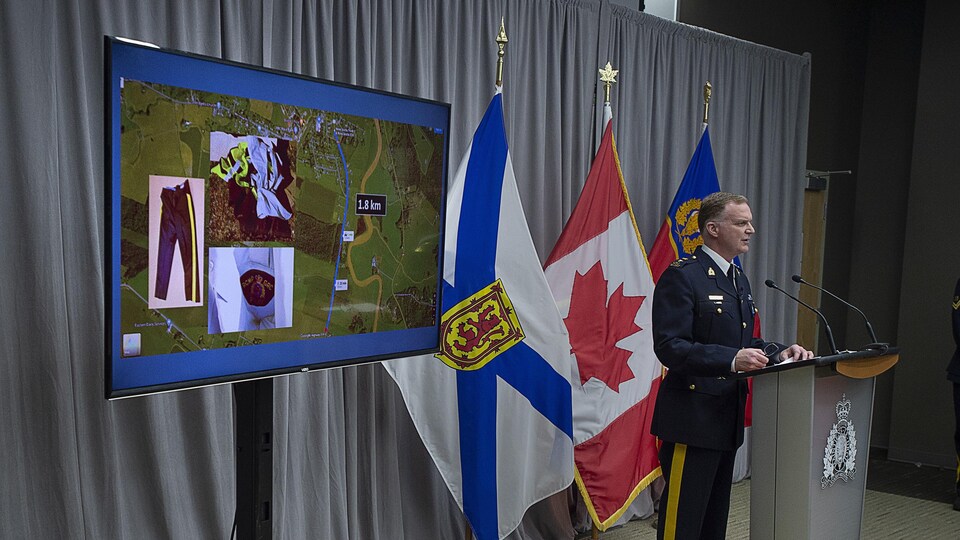 Un policier fait un point de presse près d'un écran qui affiche une carte satellitaire et des photos d'un uniforme de police.