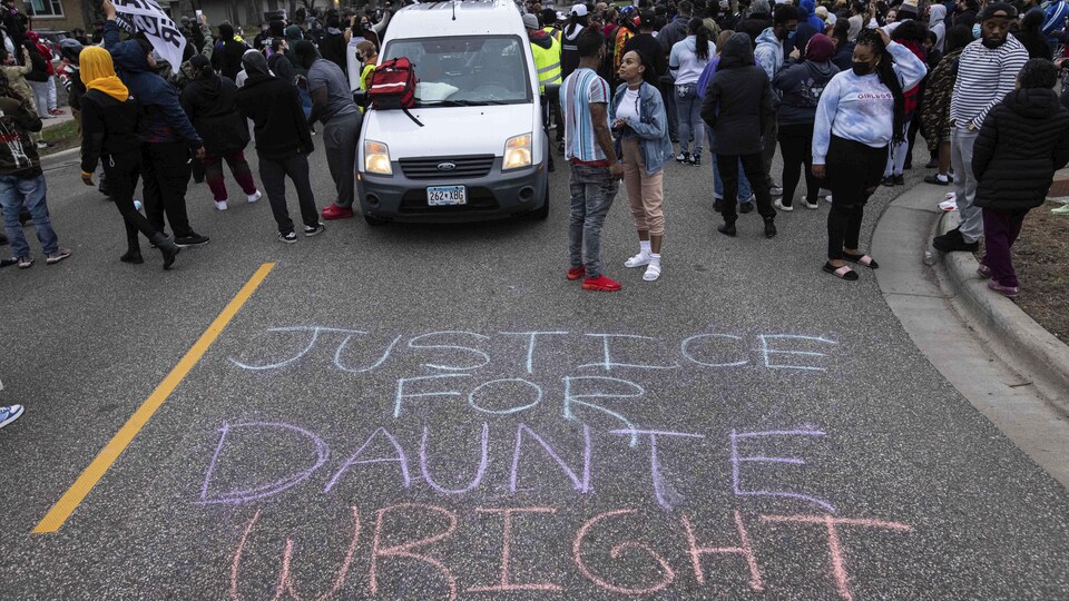 Deux jeunes discutent au cours d'une manifestation; « Justice pour Daunte Wright » est dessiné à la craie sur le sol.