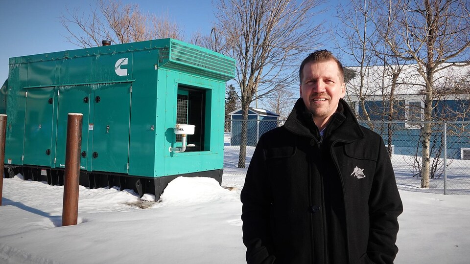 Dave Brown dehors devant un conteneur de métal vert qui abrite une génératrice.