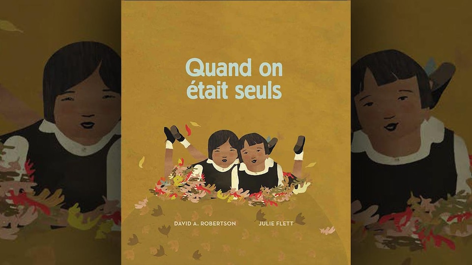 La couverture du livre Quand on était seuls, de David A. Robertson, illustré par Julie Flett. Illustration représentant deux fillettes à plat ventre sur des feuilles d'arbres, en uniforme, les pieds relevés. 