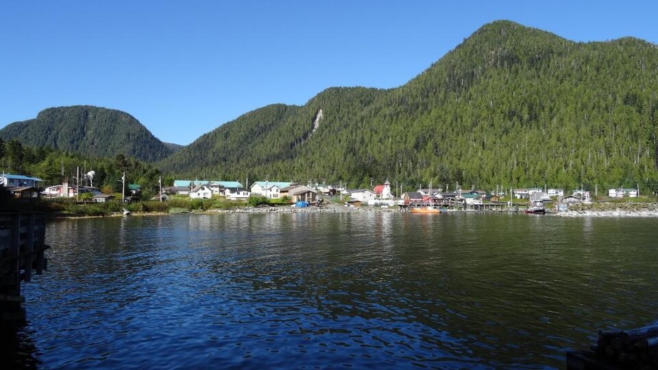 Vue de loin d'un village au bord de l'eau bordé par une montagne.