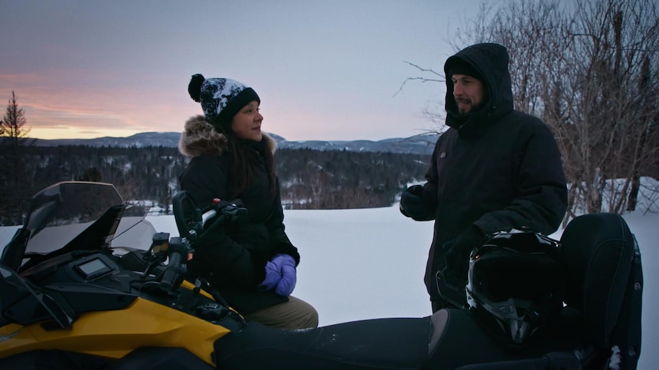 A woman and a man are talking outside, next to a snowmobile. 