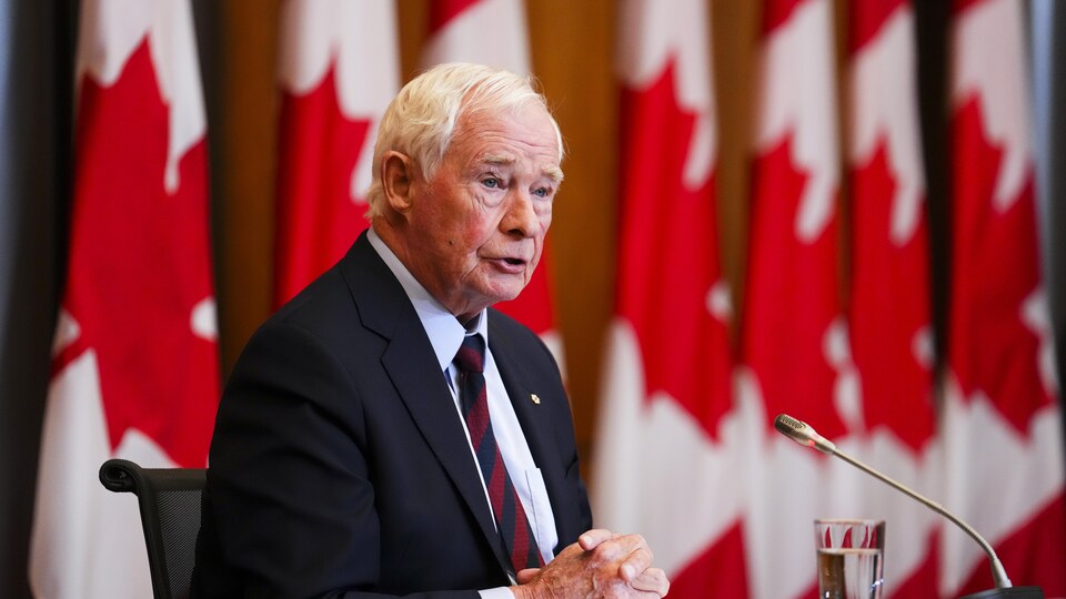 David Johnston at a press conference in front of Canadian flags.