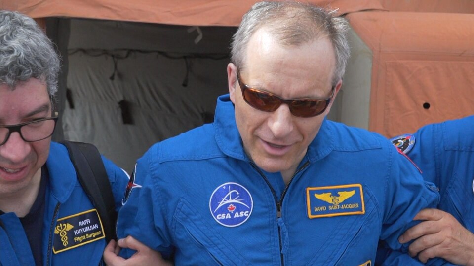 L'astronaute canadien David Saint-Jacques parle aux médias soutenu debout par des collègues.