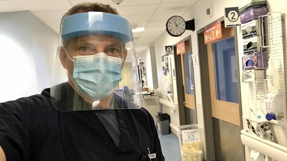David Saint-Jacques portant uniforme médical, masque et visière dans un couloir d'hôpital.