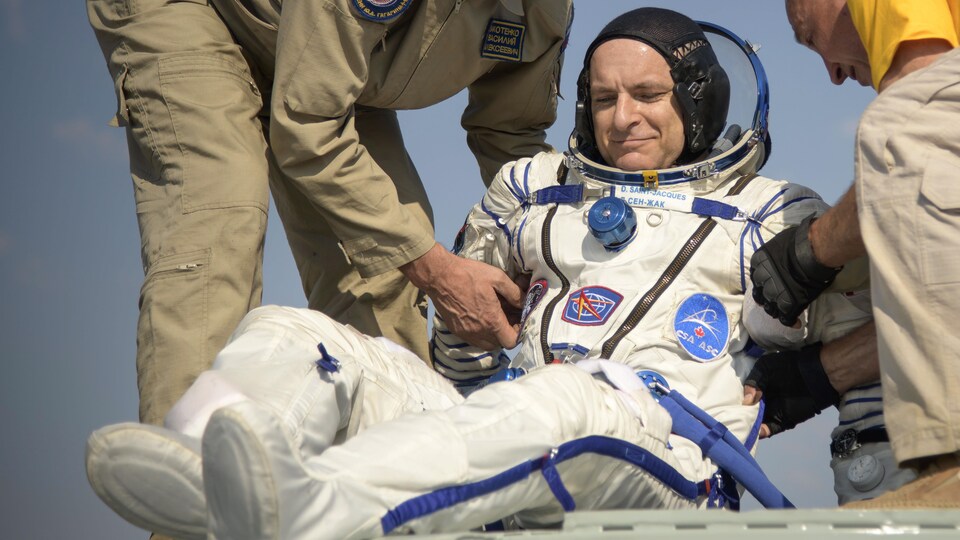 Deux hommes aident un astronaute à sortir d,une capsule spatiale.