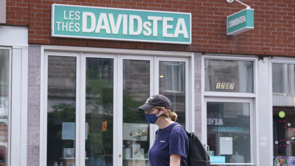 Une femme portant un masque passe devant une boutique de Davids Tea à Montréal