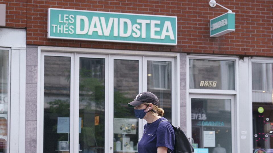 Une femme portant un couvre-visage marche devant un magasin DavidsTea.
