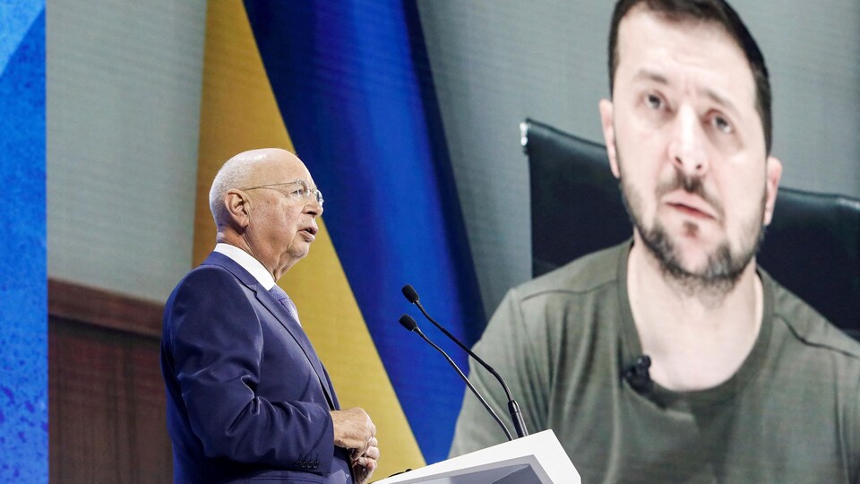Founder and Executive Chairman Klaus Schwab talks to delegates with Ukrainian President Volodymyr Zelenskiy shown on a screen in the background during the opening ceremony of the World Economic Forum. 