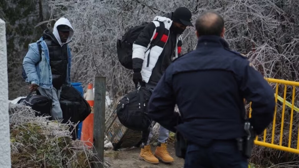Un agent de la GRC observe des migrants qui passent devant une barrière.