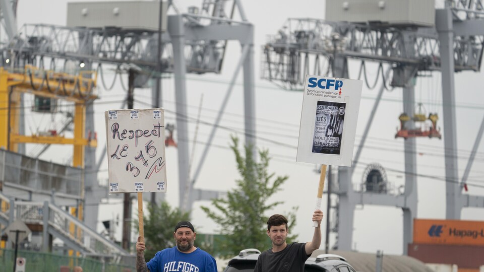 Deux grévistes brandissent des pancartes a l’entrée du port de Montréal.
