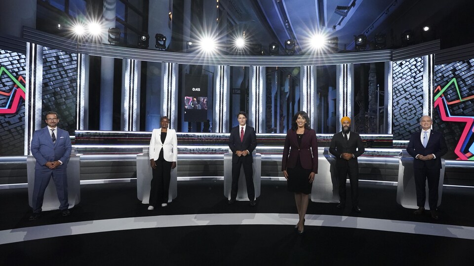 Shachi Kurl pose à l'avant-plan sur le plateau du débat, avec les chefs à l'arrière.