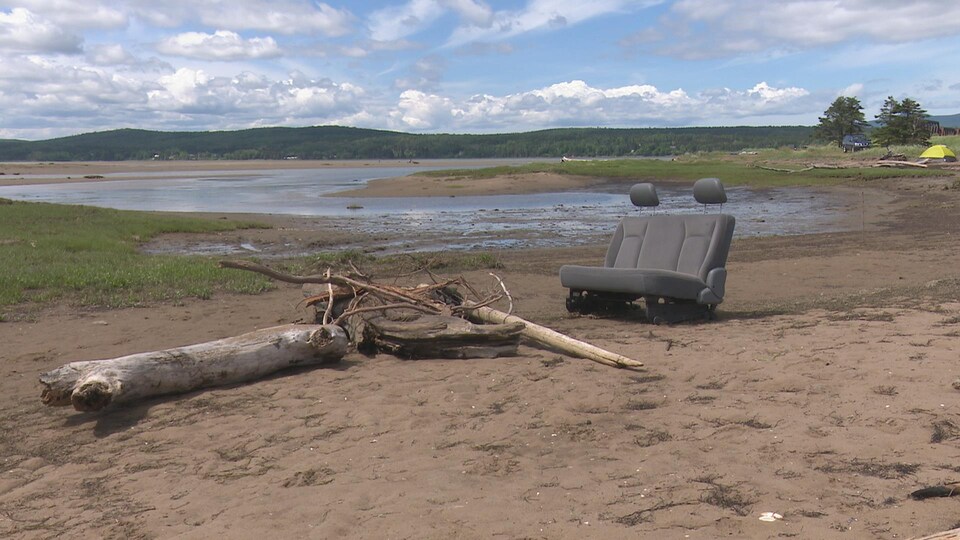 Une banquette de voiture laissée à l'abandon sur la plage, près d'un tas de branches.