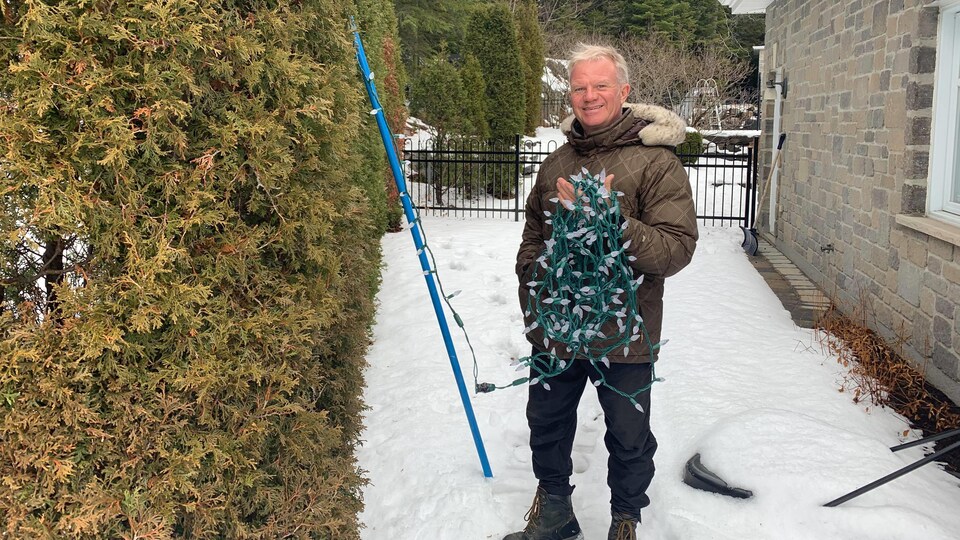 Un homme tient des lumières de Noël à l'extérieur de sa maison.