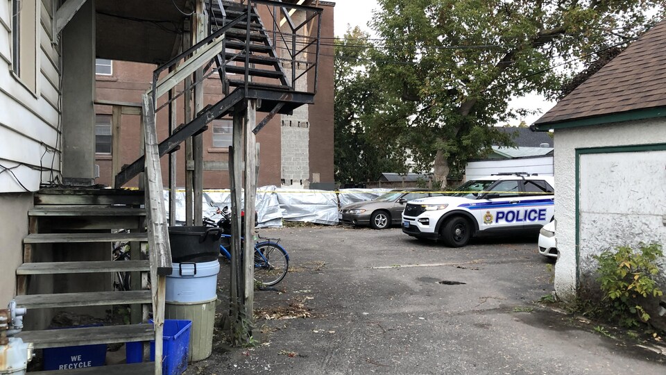 Une voiture de la police d'Ottawa est stationnée derrière un immeuble à logements par un matin nuageux.
