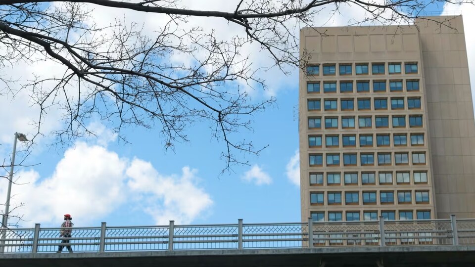 Une personne marchant sur un viaduc, devant une tour à bureaux. 