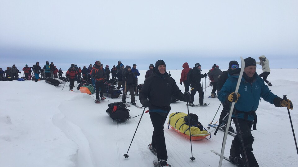 Des dizaines de personnes marchent avec leurs bagages sur le lac Saint-Jean.