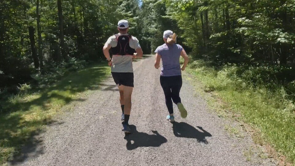 Un homme et une femme courent dans un sentier au milieu d’une forêt, devant un cycliste.