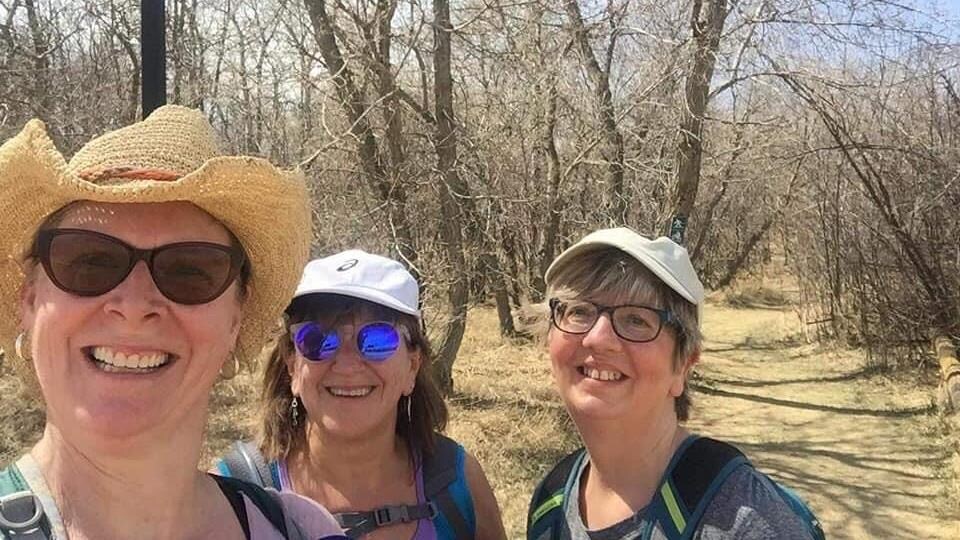 Trois femmes prennent un selfie vêtues de chapeaux, de lunettes de soleil et de sacs à dos.