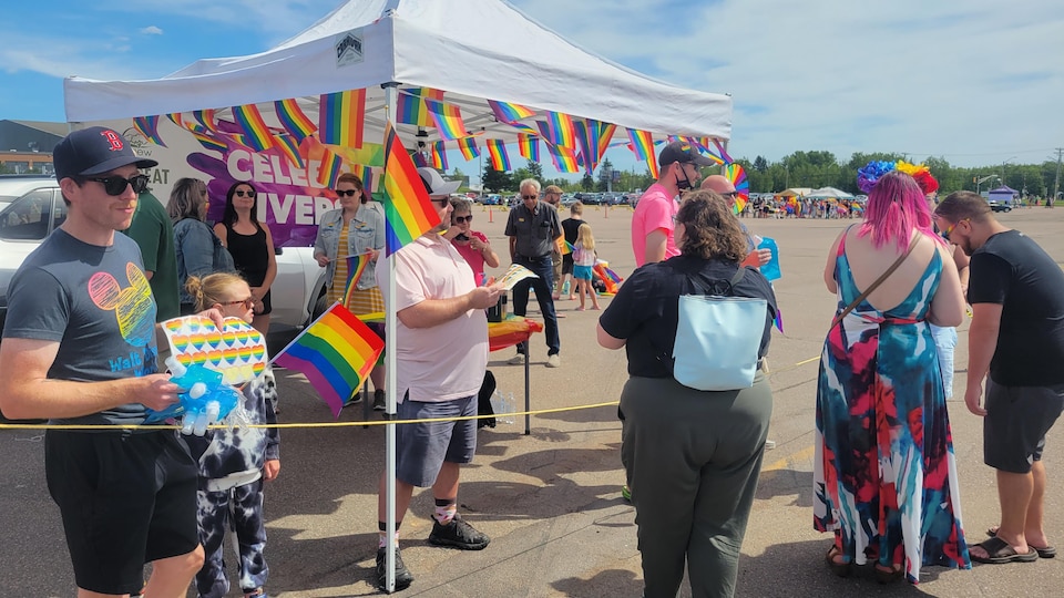 Des gens de tout âge réunis sous un chapiteau garni de drapeaux arc-en-ciel.