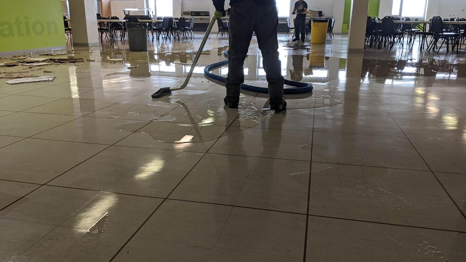 Deux personnes aspirent l'eau sur le plancher avec l'aide d'aspirateur.