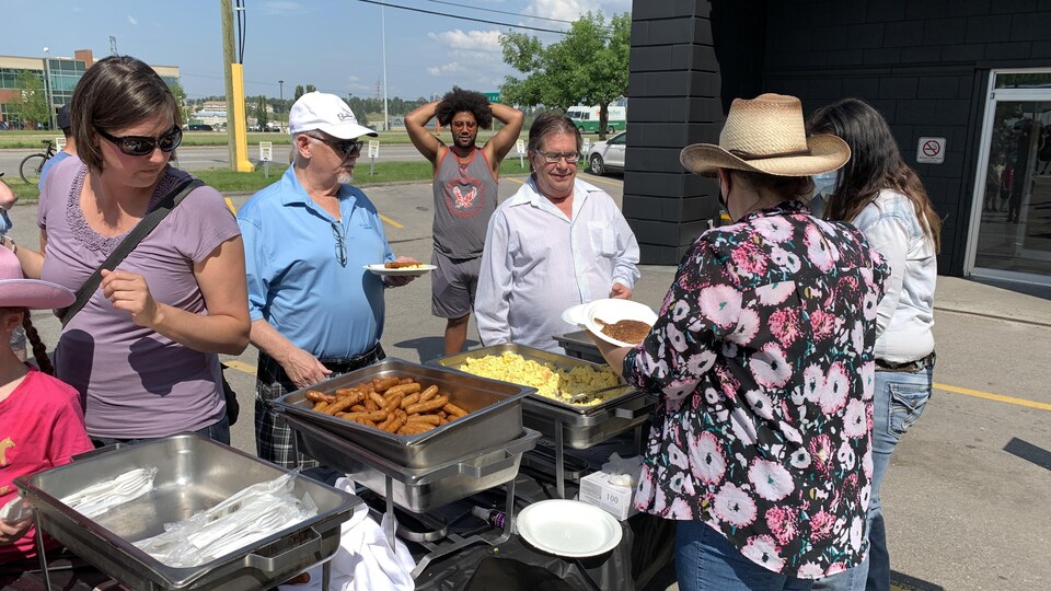 Des personnes se font servir des oeufs brouillés et des saucisses en plein air.
