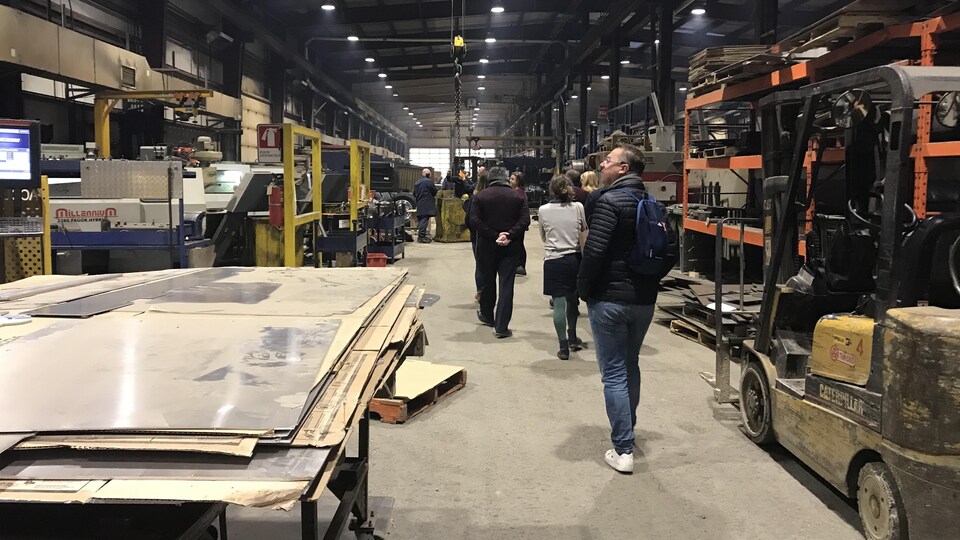 Des personnes se promènent dans la salle d'une usine avec de grands morceaux de bois.  