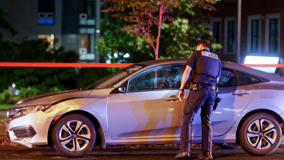 Un policier regarde à l'intérieur d'une voiture accidentée la nuit.