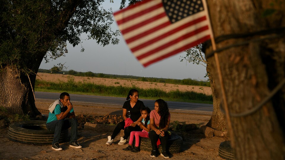 Un homme, une femme, une adolescente et une jeune fille attendent sur des pneus. Un drapeau des États-Unis flotte, accroché à un arbre. 