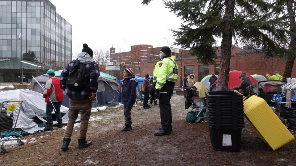 Un policier surveille des gens dans un campement de fortune.