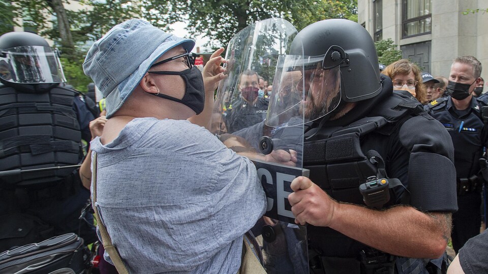 Un policier en combinaison antiémeute utilise son bouclier pour pousser un homme d'un certain âge.