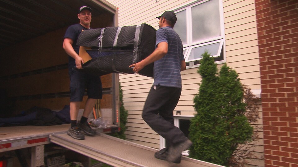 Deux hommes transportent un meuble sur la rampe d'un camion de déménagement.