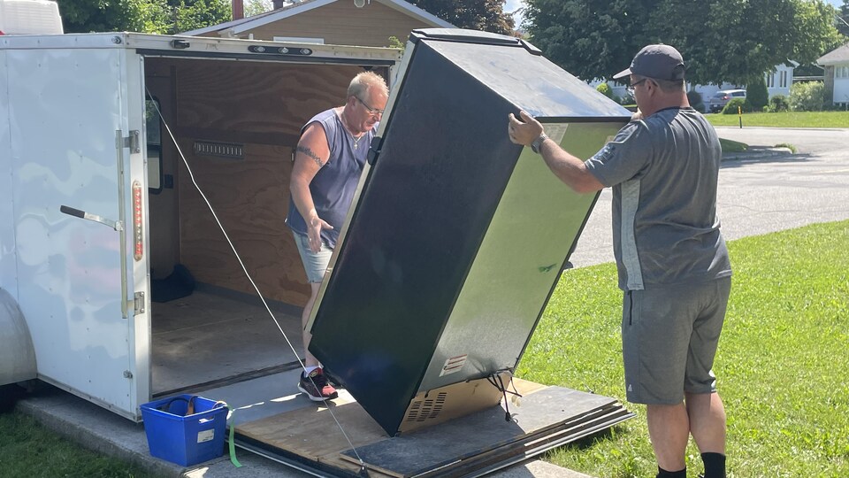 Deux hommes déplacent un frigo dans une fourgonnette.