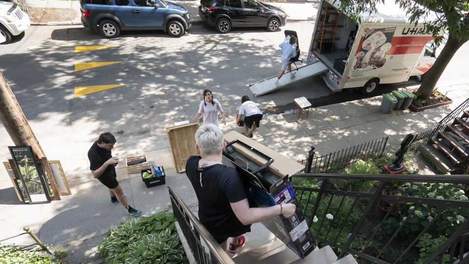 Une personne descend un escalier en tenant une boîte, tandis que d'autres remplissent un camion stationné dans la rue.