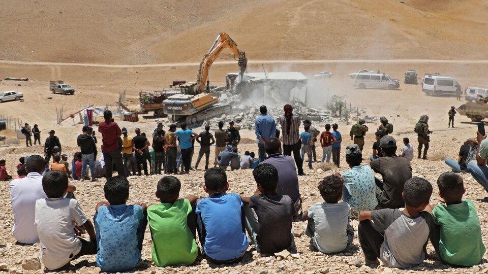Des villageois assistent à la démolition d'une maison.