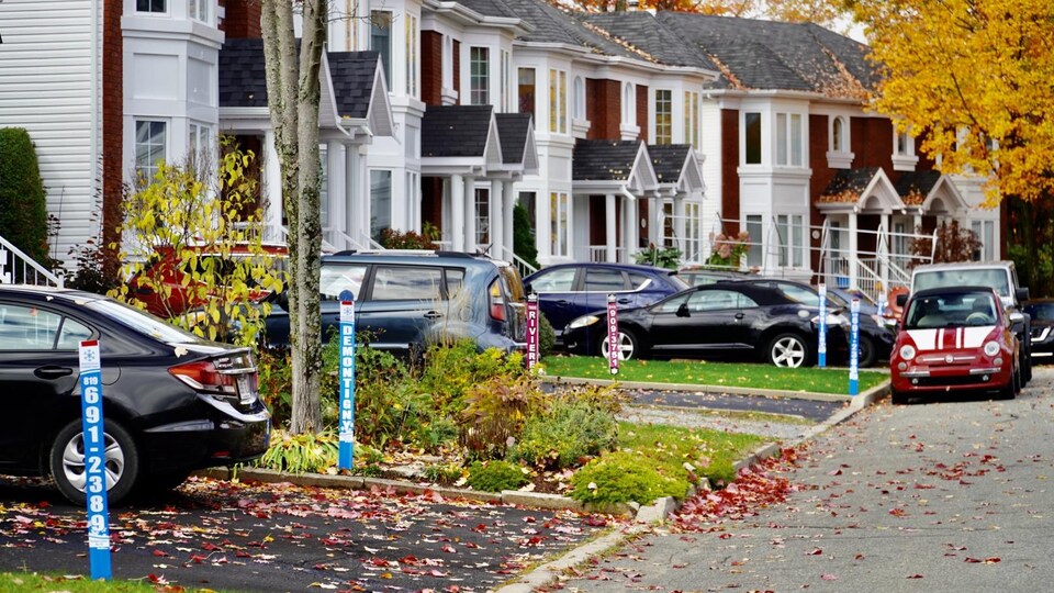 Des balises de déneigeurs plantées sur des terrains de clients, à côté de voitures stationnées.