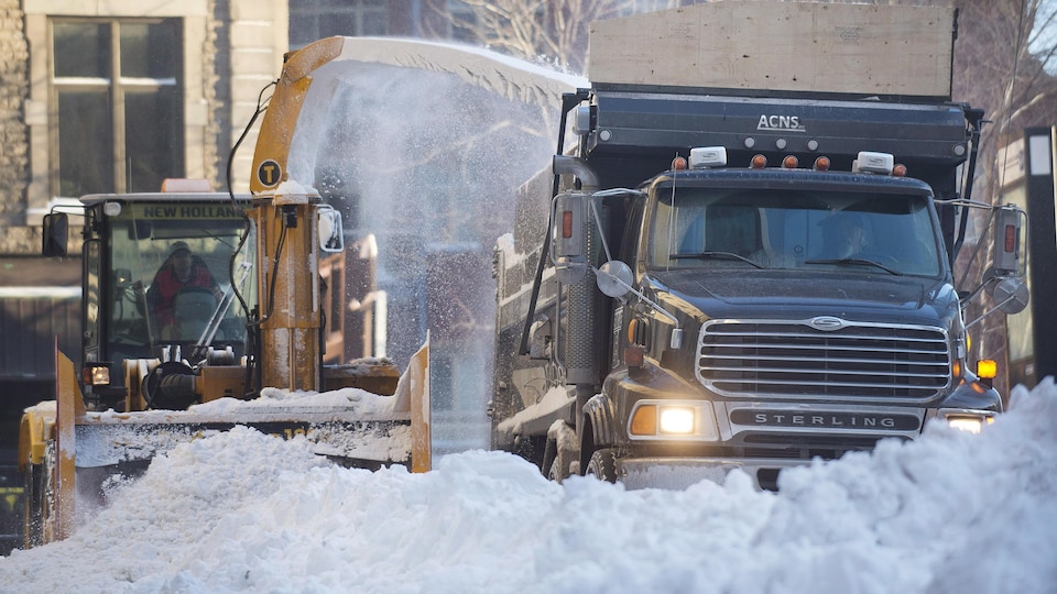 Un déneigeur souffle de la neige dans un camion de chargement, à ses côtés.